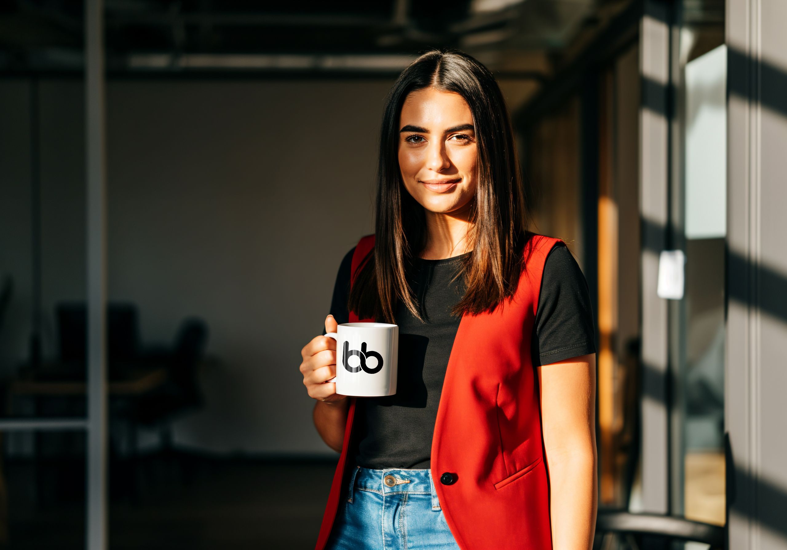 Woman in black shirt and red sleeveless vest holding a mug with Baden Bower mug smiling.